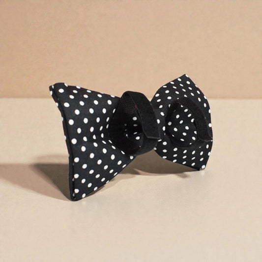 Black detachable dog bow tie with white polka dots on a beige background