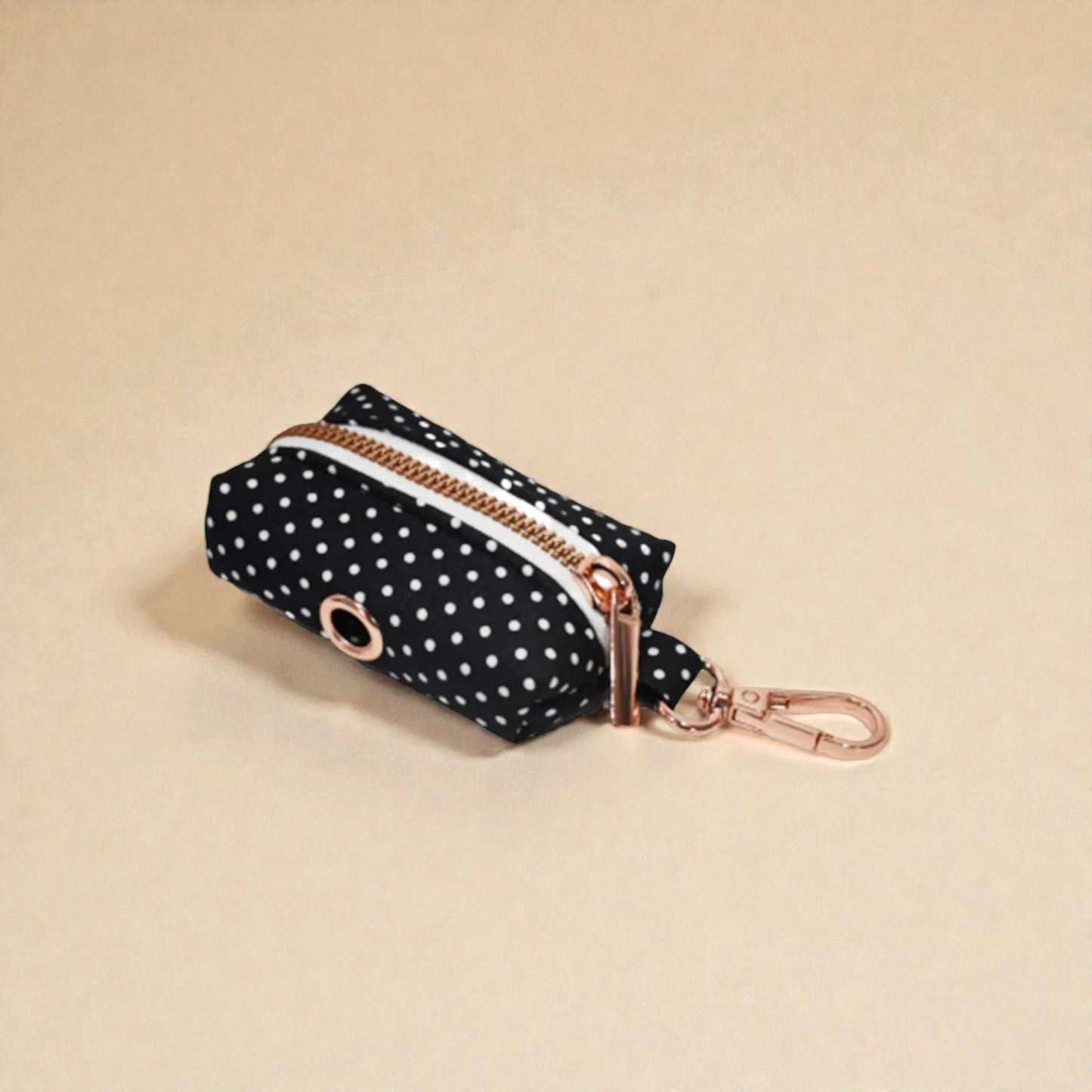 Black polka dot dog poop bag holder with gold zip and clip on a beige background
