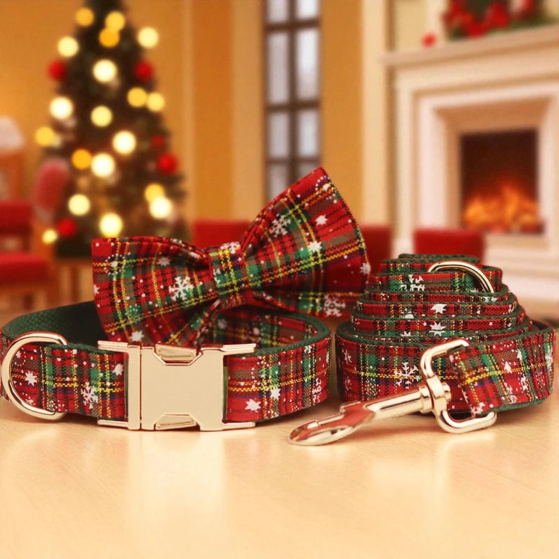 Red and green plaid dog collar and lead set with a bow tie on a table in front of a Christmas tree and fireplace.