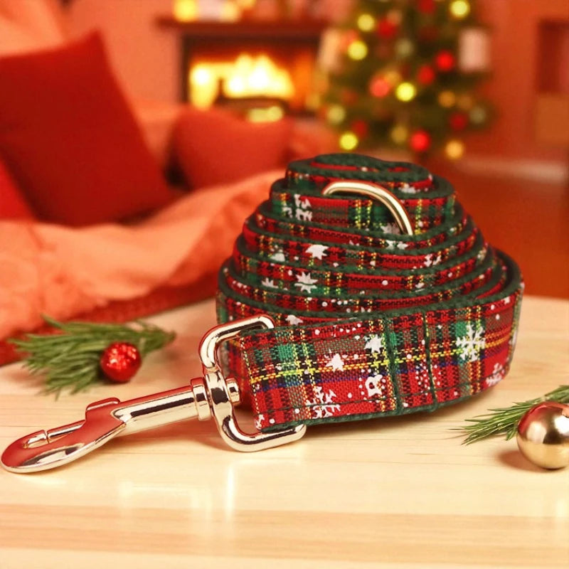 Red and green plaid dog lead with silver clasp on a wooden surface, Christmas tree and decorations in the background.