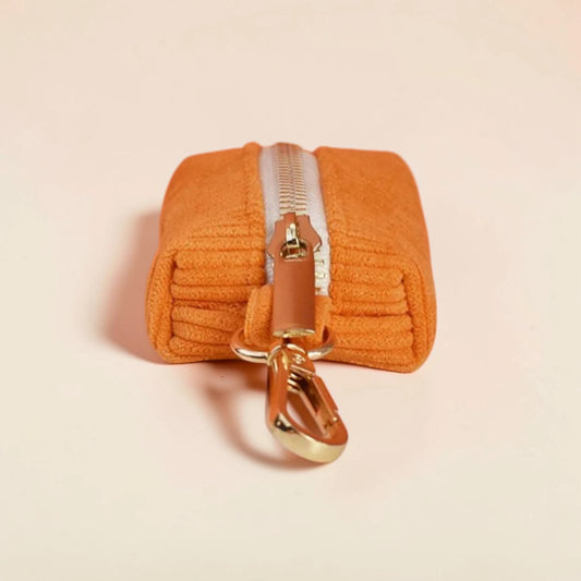 Orange dog poop bag holder with a gold zip on a beige background