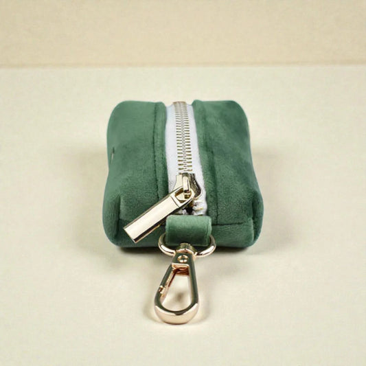 Green dog poop bag holder with a gold zip and clip on a beige background