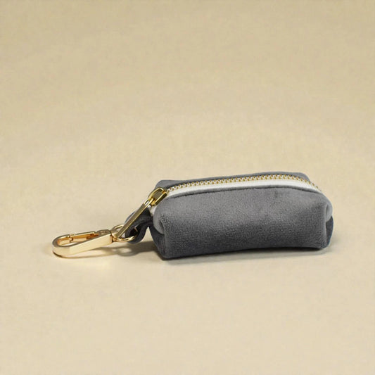 Grey velvet dog poop bag holder with gold zip and clip on a beige background
