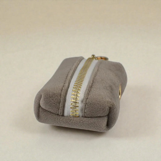 Grey dog poop bag holder with a gold zip on a beige background