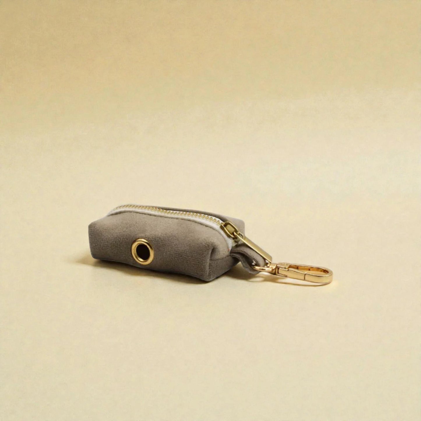 Grey dog poop bag holder with gold zip and clip on a beige background