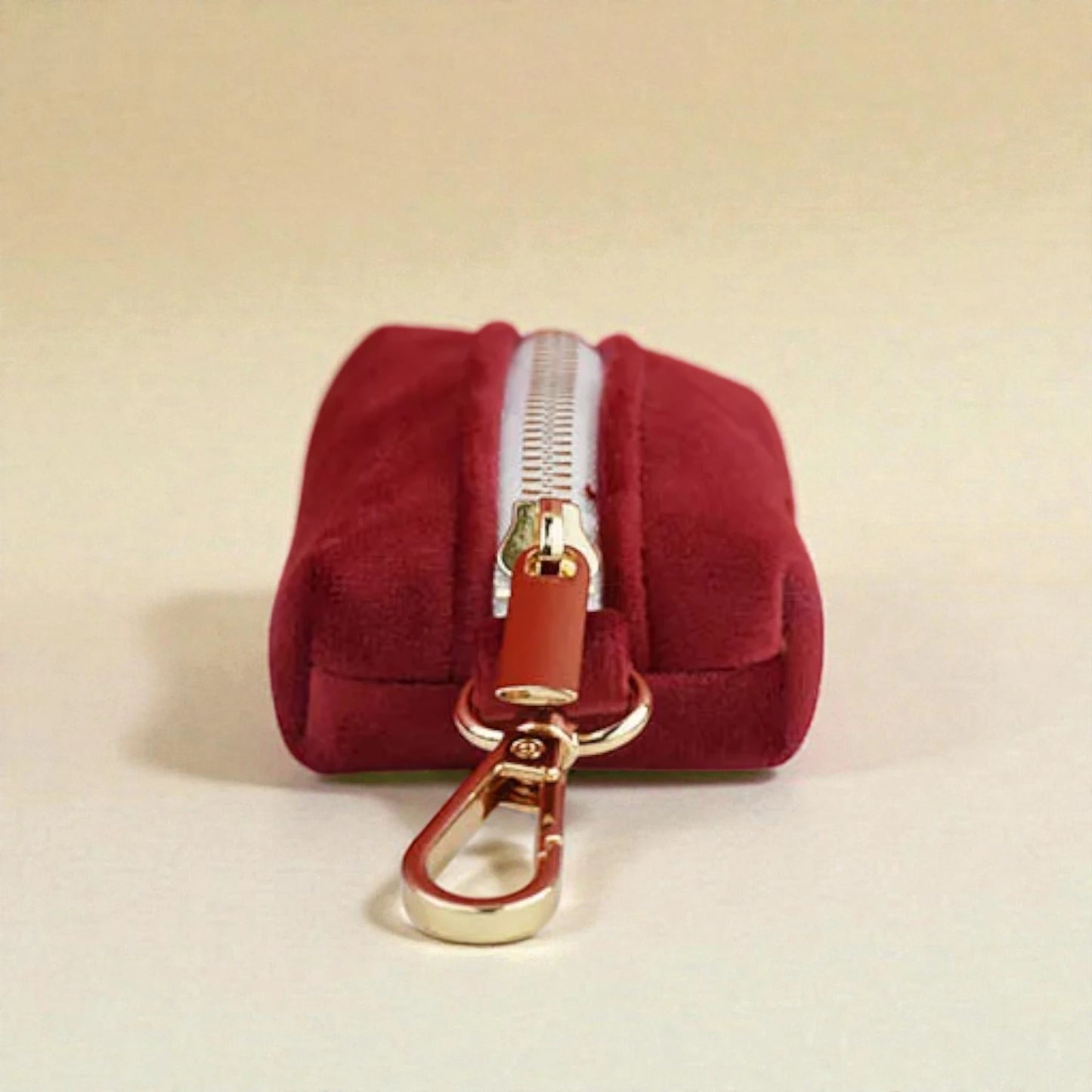 Red dog poop bag holder with a gold zip and clip on a beige background