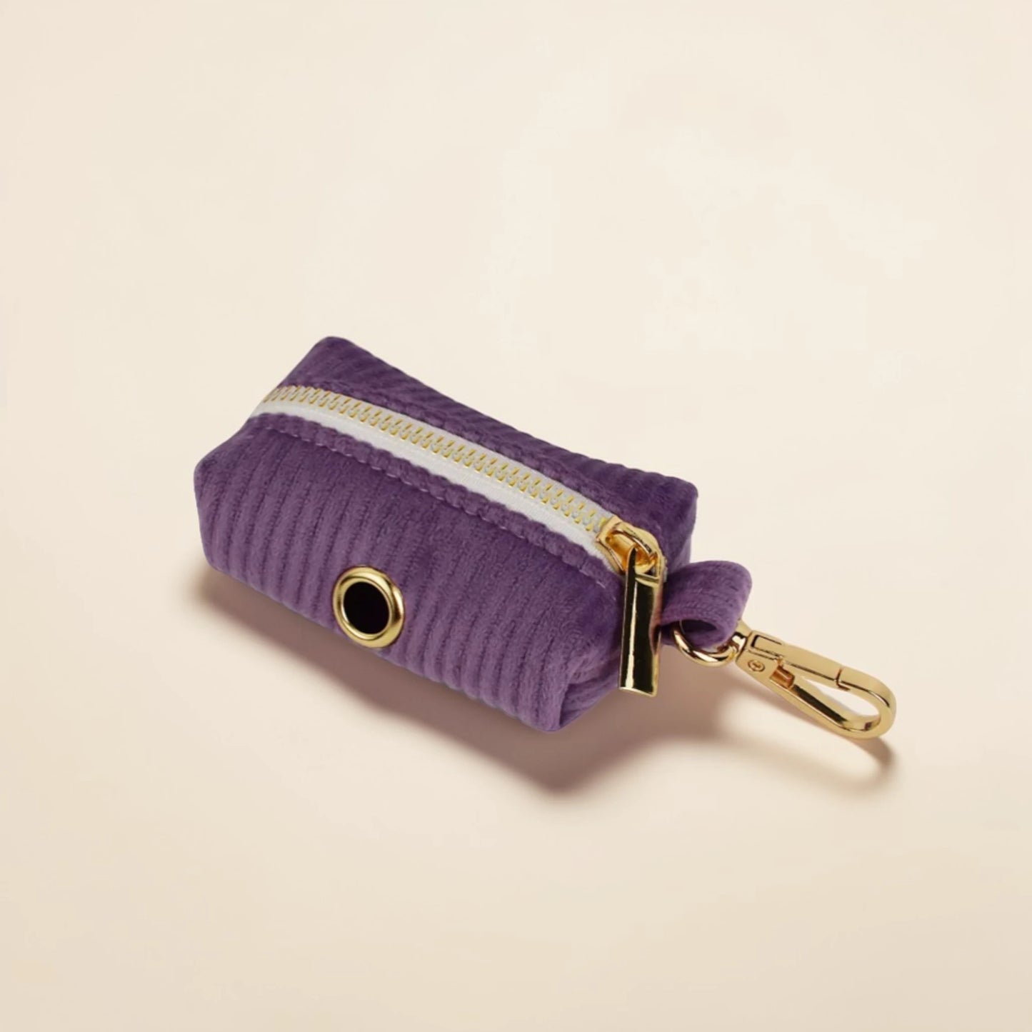 Purple corduroy dog poop bag holder with gold zip and clip on a beige background