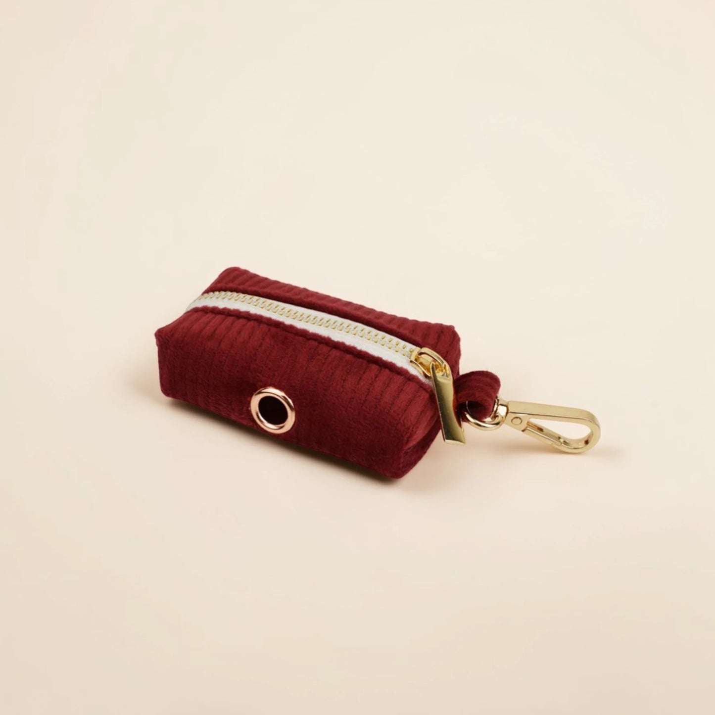 Red corduroy dog poop bag holder with gold zip and clip on a beige background