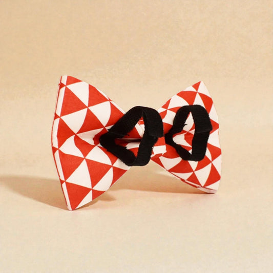 Red and white geometric patterned dog bow tie on a beige background