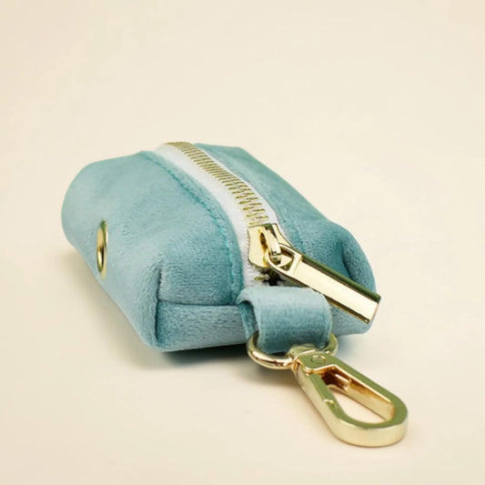 Teal blue dog poop bag holder with gold zip and carabiner clip on a beige background