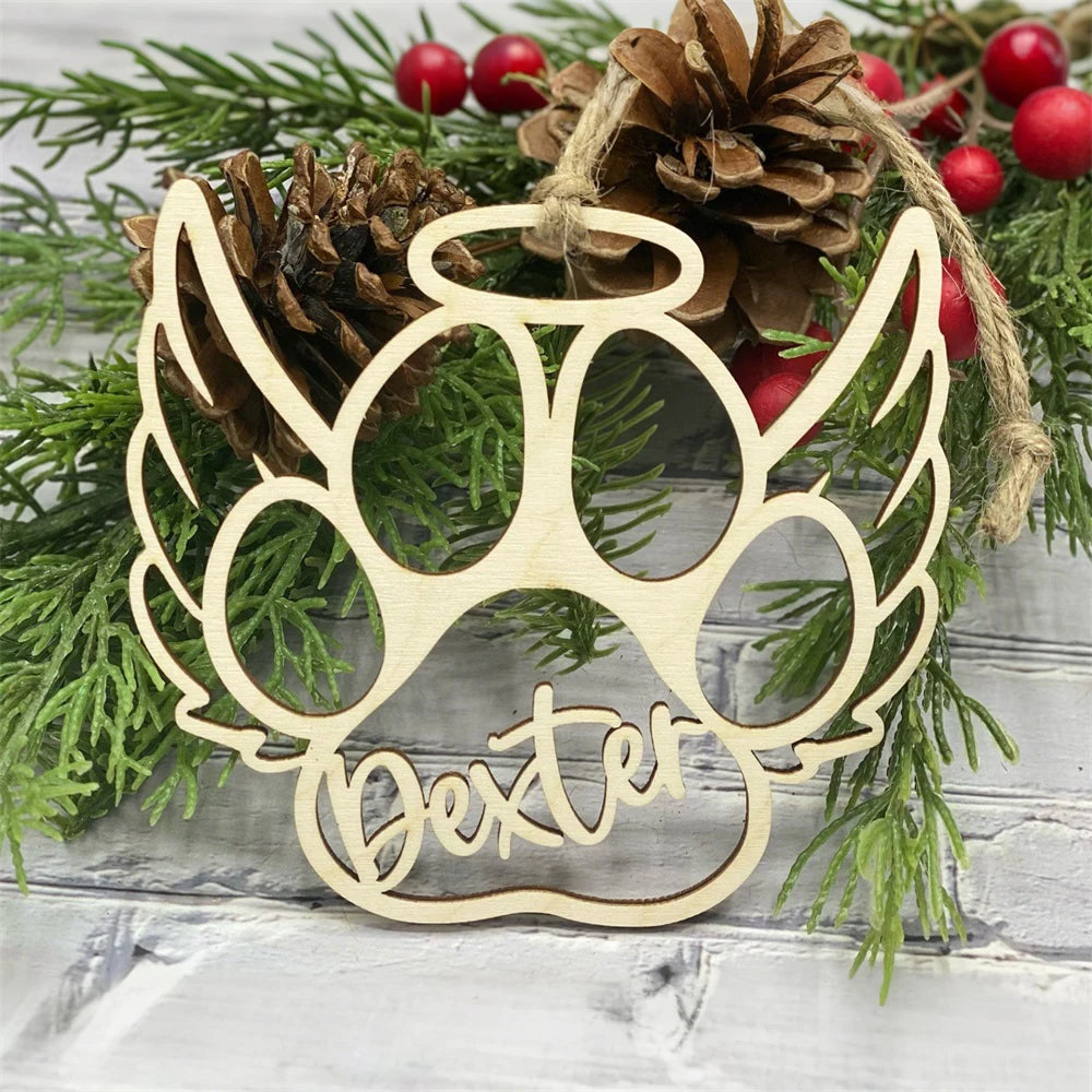 Wooden paw print ornament with 'Dexter' engraved, surrounded by Christmas greenery and pinecones.