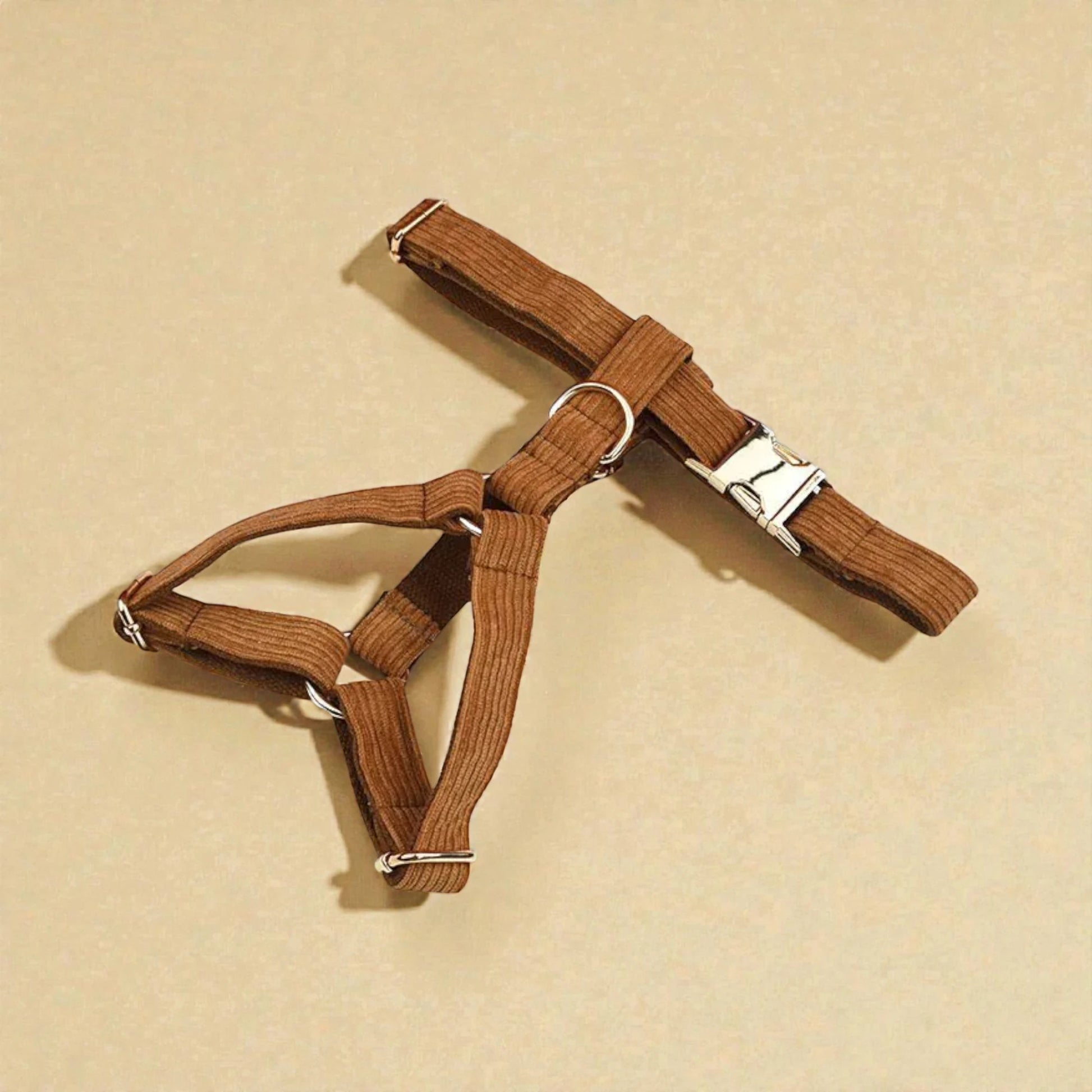 Brown dog harness with metal buckle on a beige background