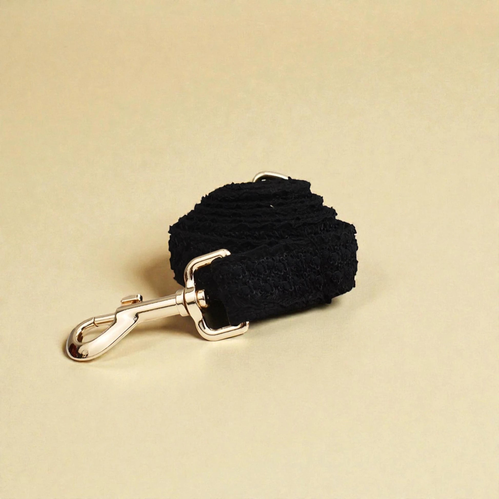 Black lace dog lead with gold clip on a beige background