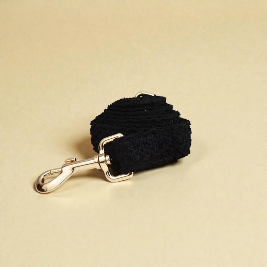 Black lace dog lead with gold clip on a beige background