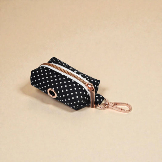 Black polka dot dog poop bag holder with gold zip and clip on a beige background