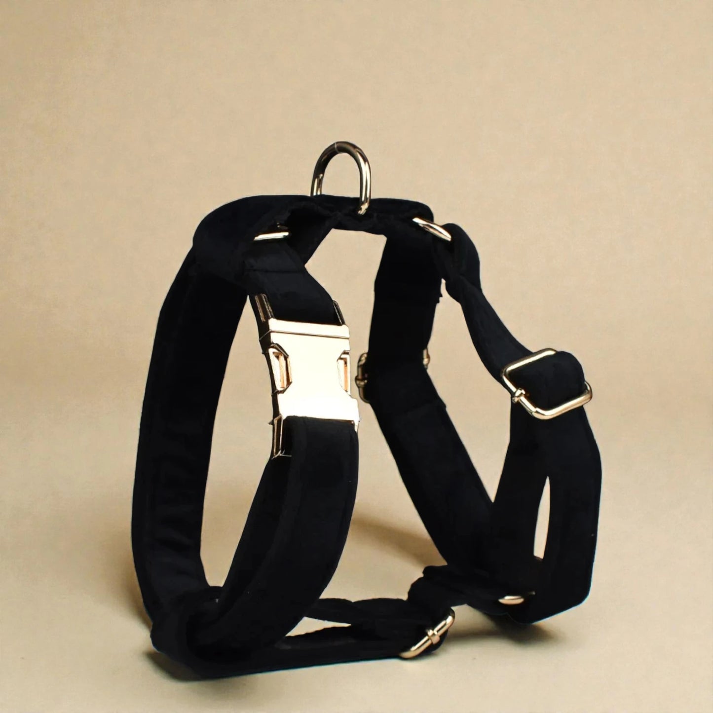 Black dog harness with metal hardware on a beige background