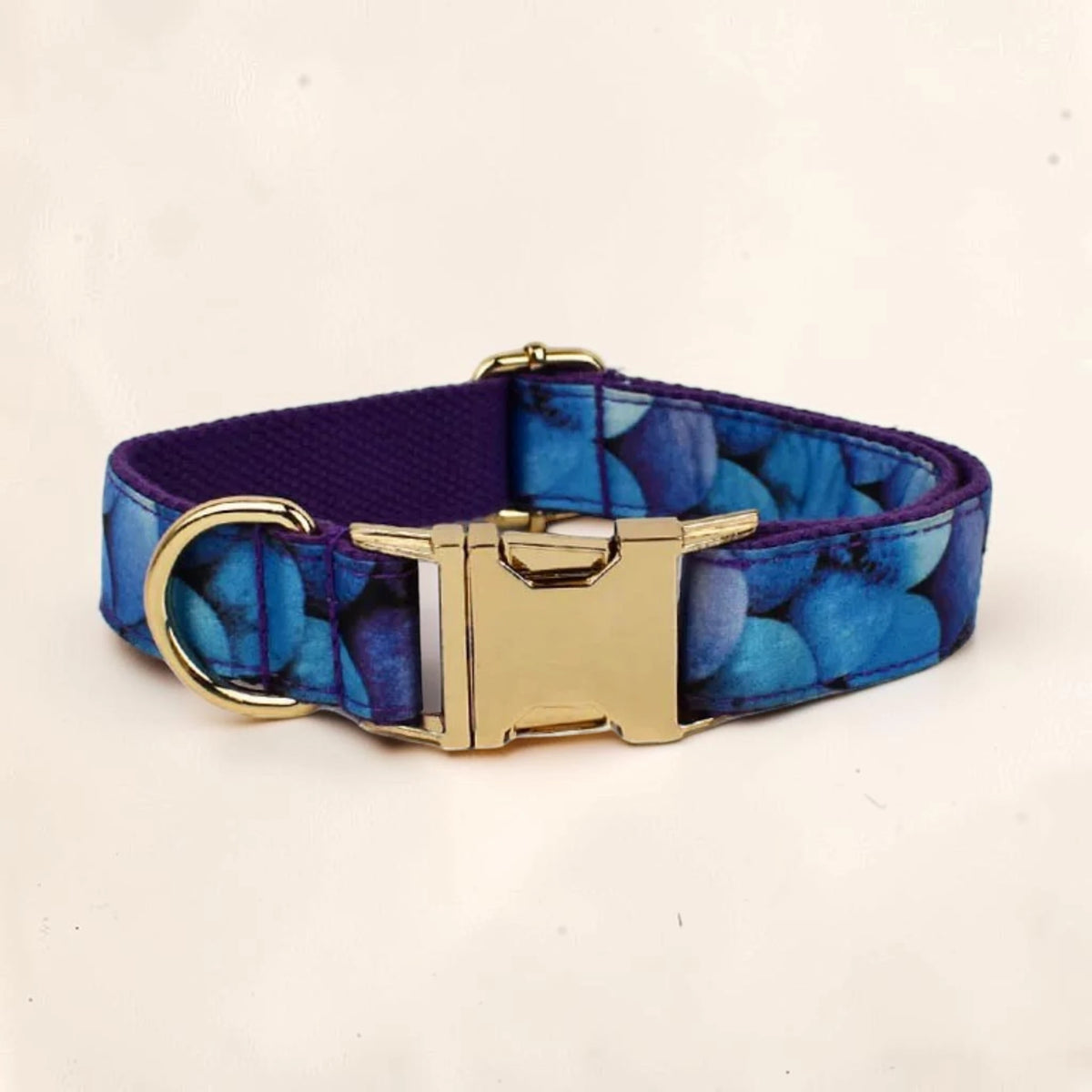 A dog collar with a blue pattern and a gold-tone metal buckle and D-ring, shown on a light beige background. Can  be personalised.