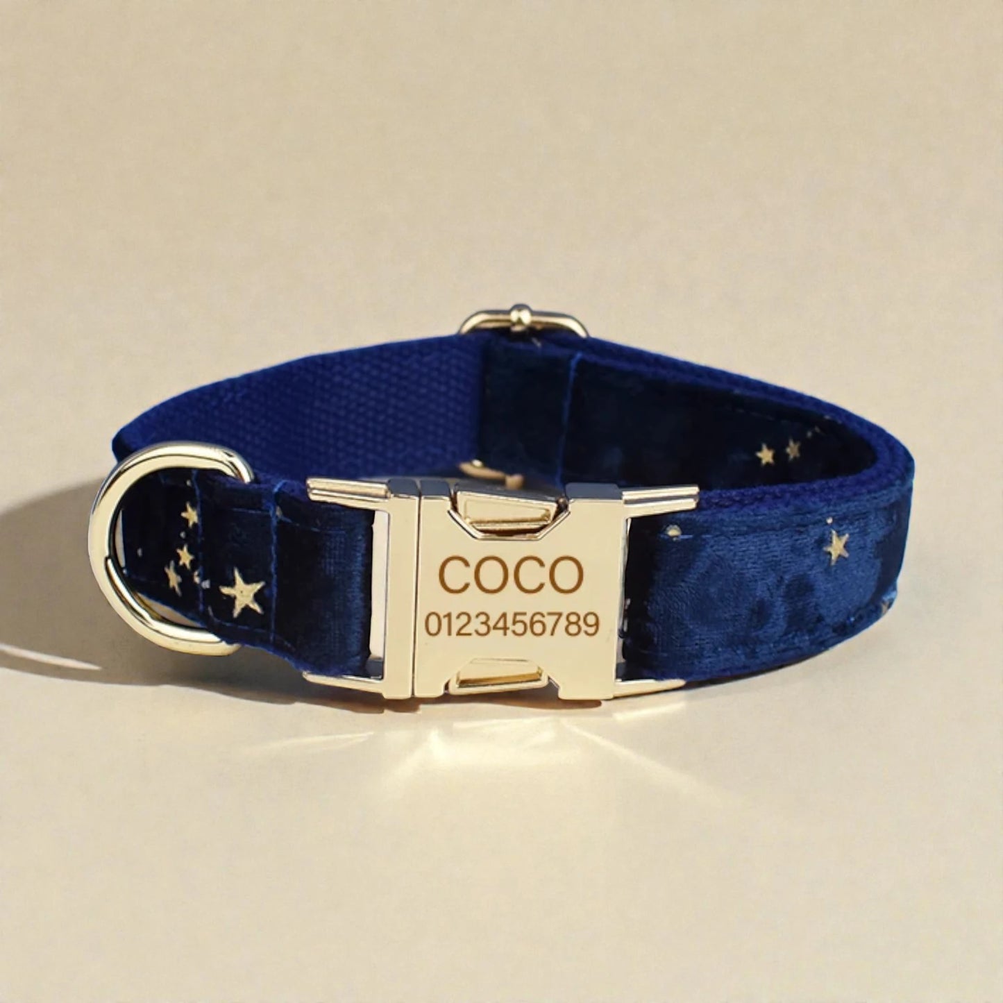 Navy blue dog collar with gold buckle and engraved nameplate on a beige background