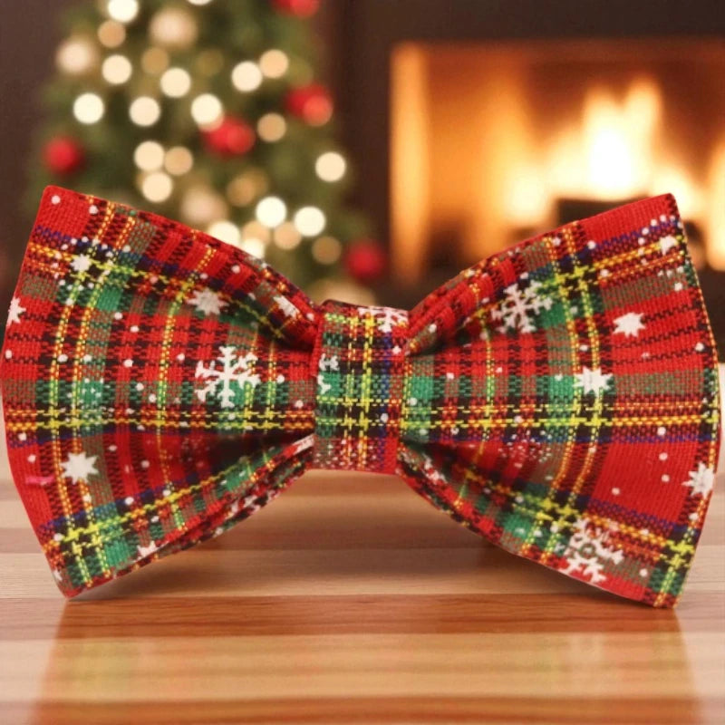 Plaid bow tie with Christmas-themed patterns on a wooden surface, blurred Christmas tree and fireplace in the background.