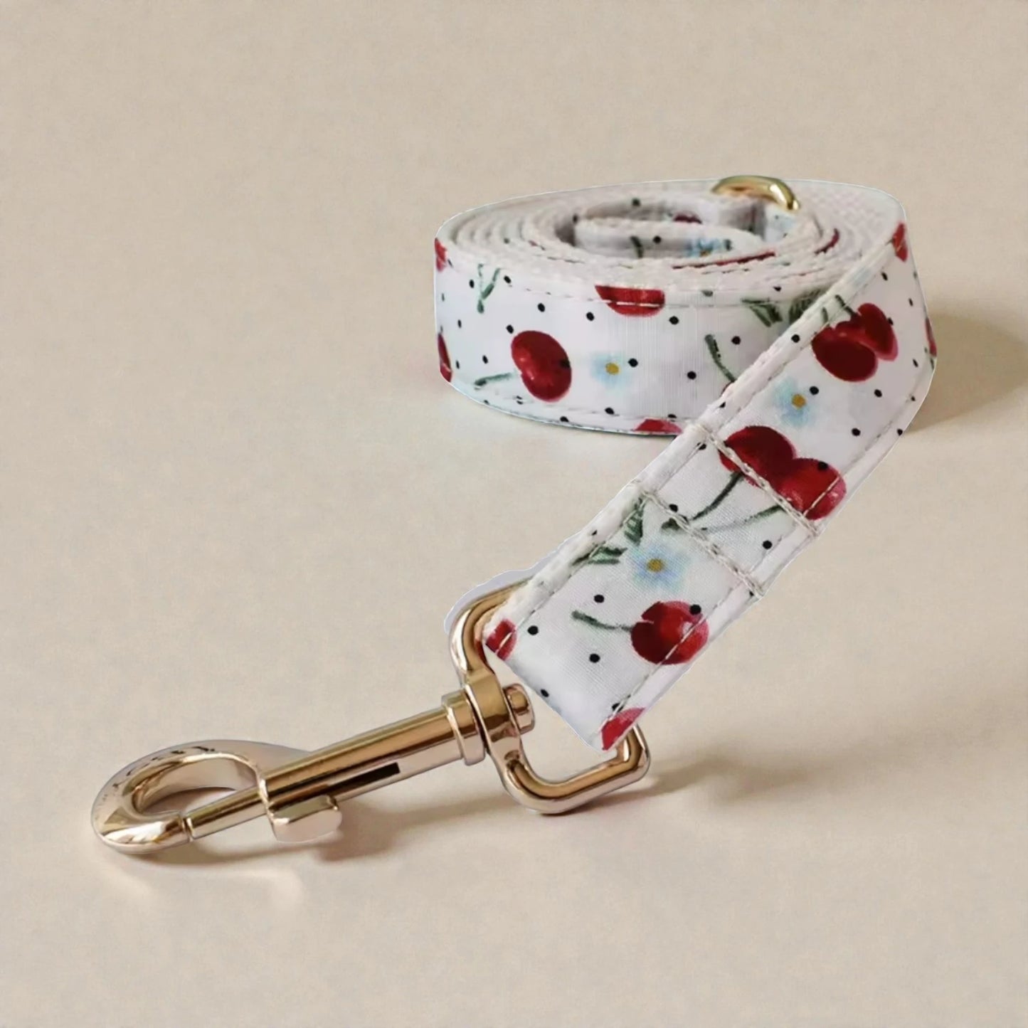 Floral red cherry patterned dog lead with a gold clip on a beige background