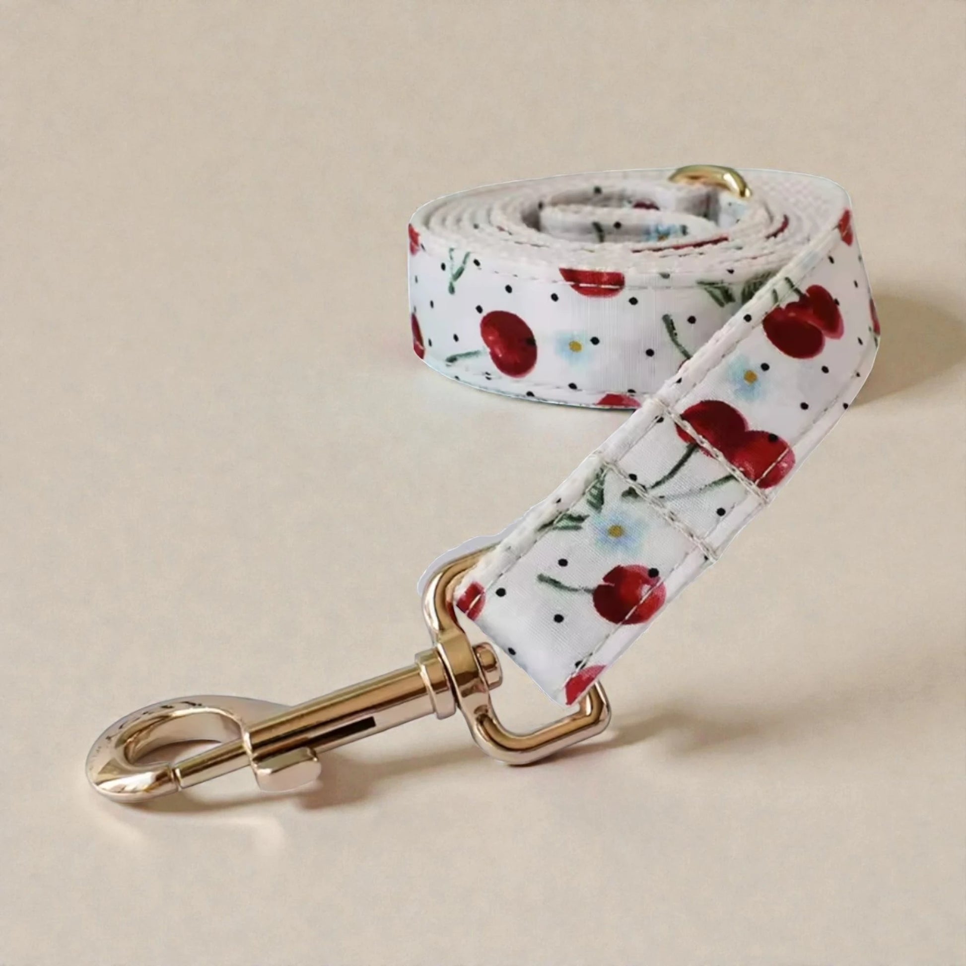 Floral red cherry patterned dog lead with a gold clip on a beige background