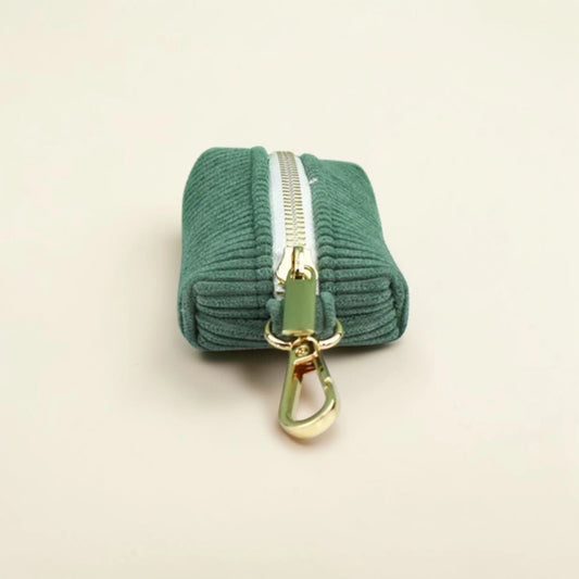 Green corduroy dog poop bag holder with gold zip and clip on a beige background