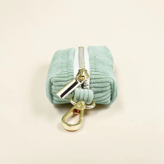 Light green dog poop bag holder with gold zip and clip on a beige background