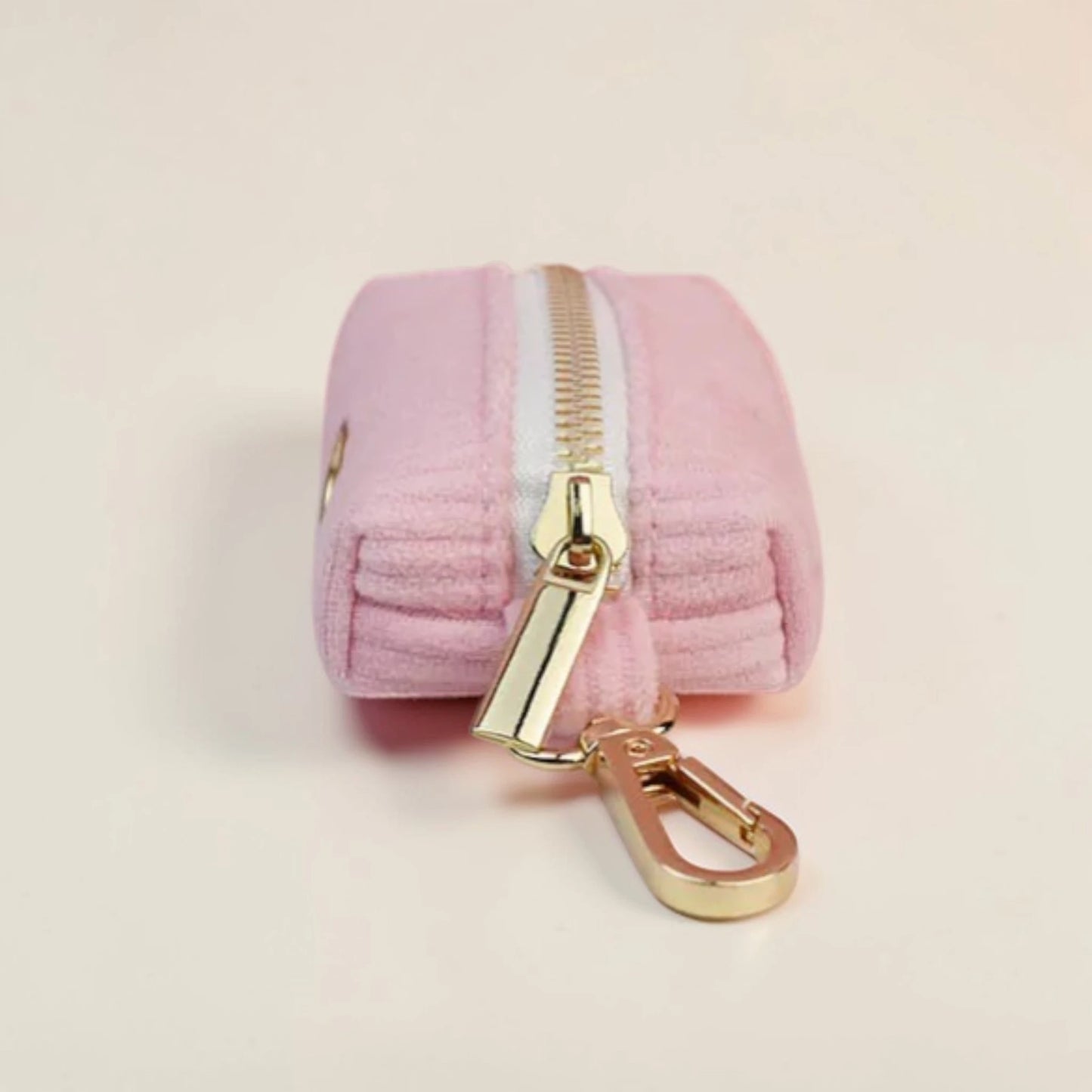 Pink dog poop bag holder with gold zip and clip on a beige background