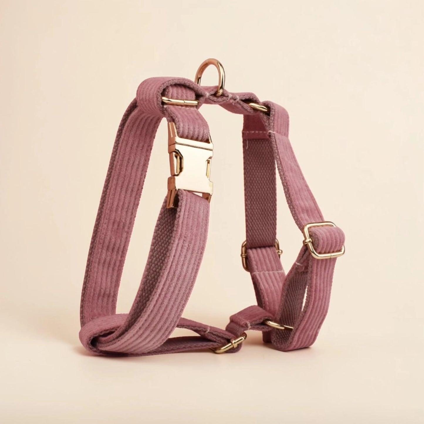 Powder pink dog harness with gold hardware on a beige background