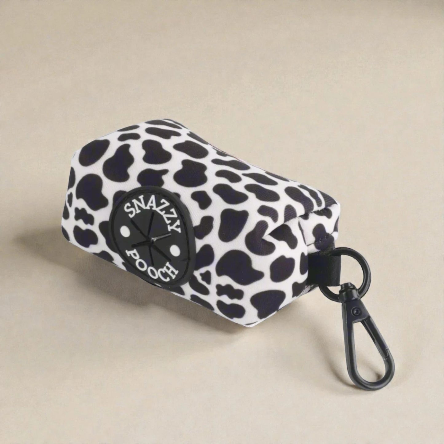 Cow print poop bag holder with 'Snazzy Pooch' logo on a beige background