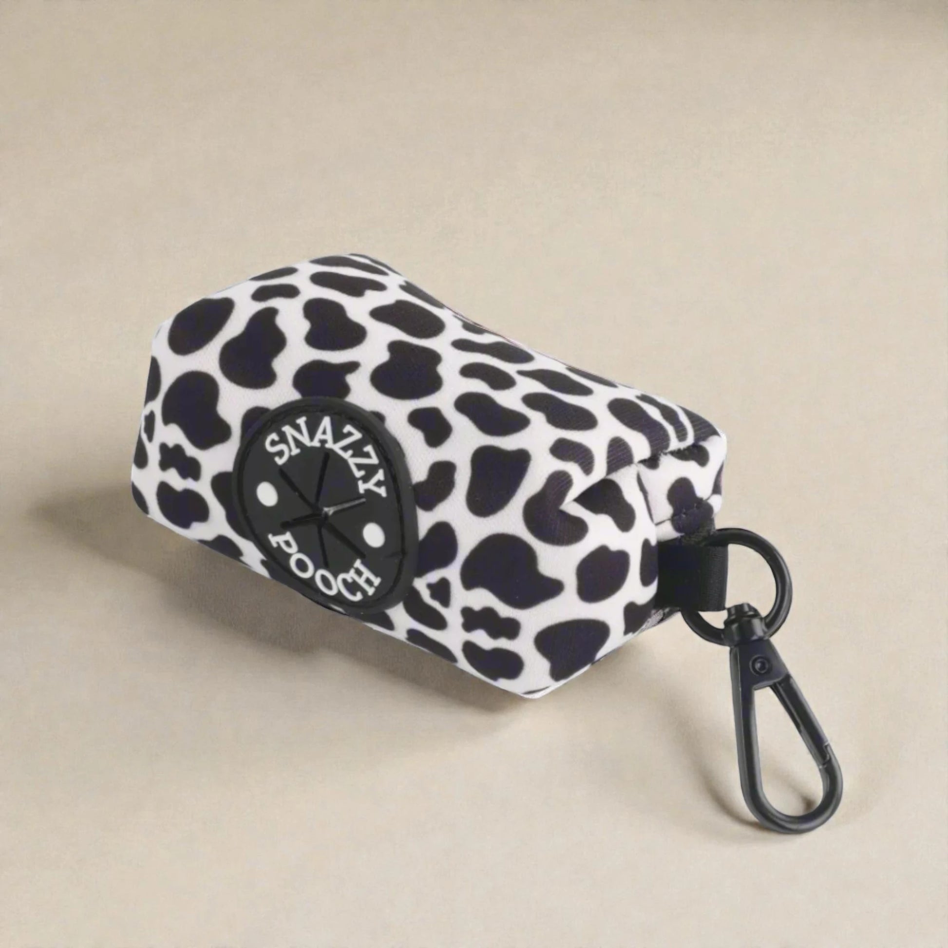 Cow print poop bag holder with 'Snazzy Pooch' logo on a beige background