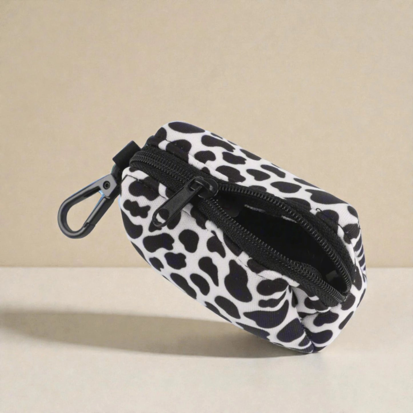 Dog poop bag holder with black and white pattern and a clip on a beige background