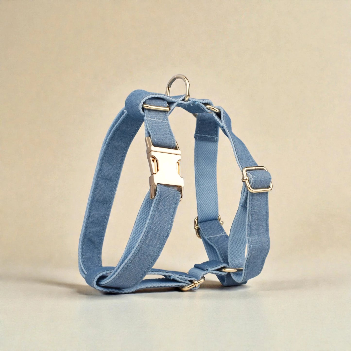 Denim blue dog harness with gold hardware on a beige background