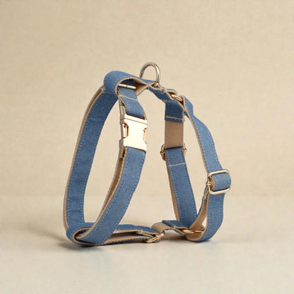 Blue denim dog harness with gold hardware on a beige background