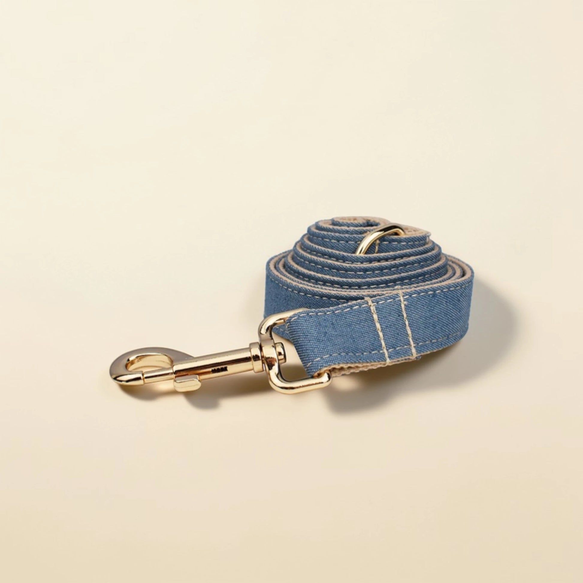 Denim tan dog lead with gold hardware on a beige background