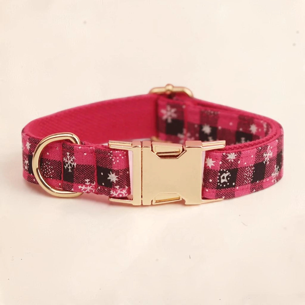 A pink plaid dog collar with white snowflake patterns and a gold-tone metal buckle and D-ring and can be personalised.