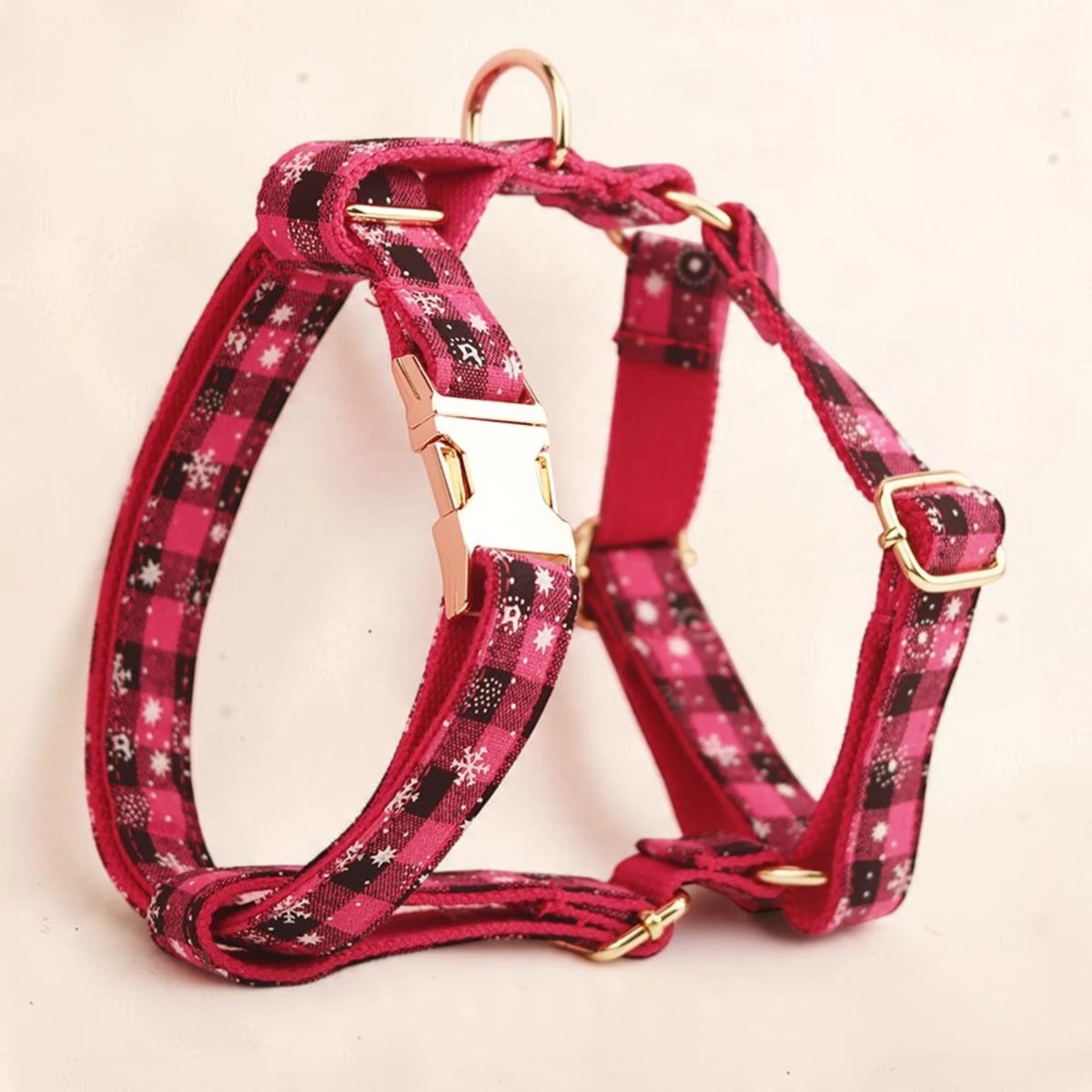 A pink plaid dog harness with white snowflake patterns and gold-tone metal hardware. Buckle can be personalised.