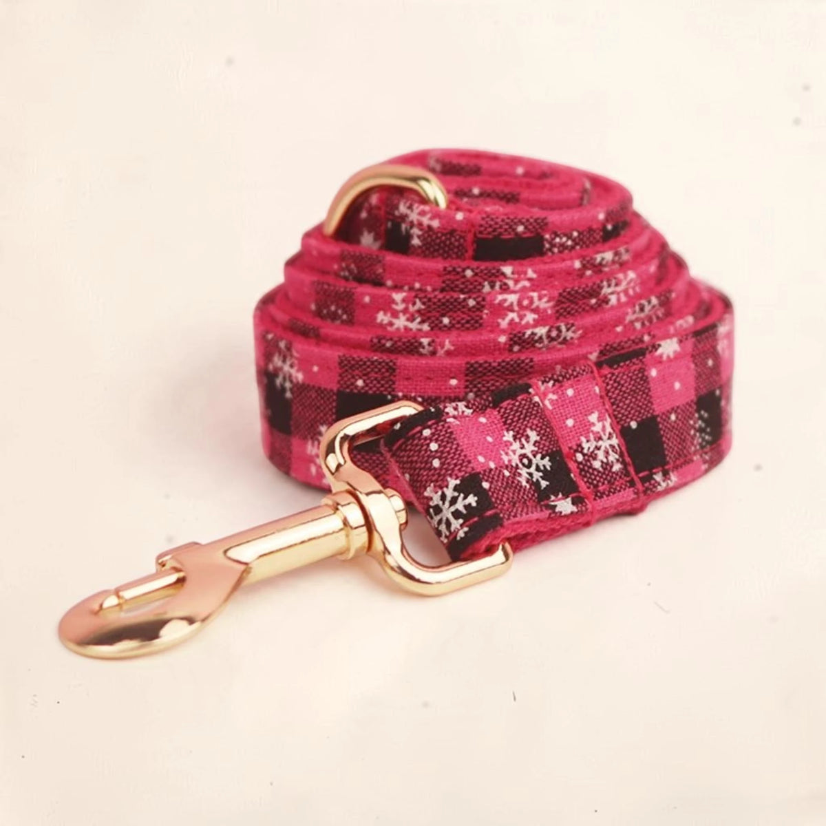 A pink plaid dog lead with white snowflake patterns and a gold-tone metal clasp.