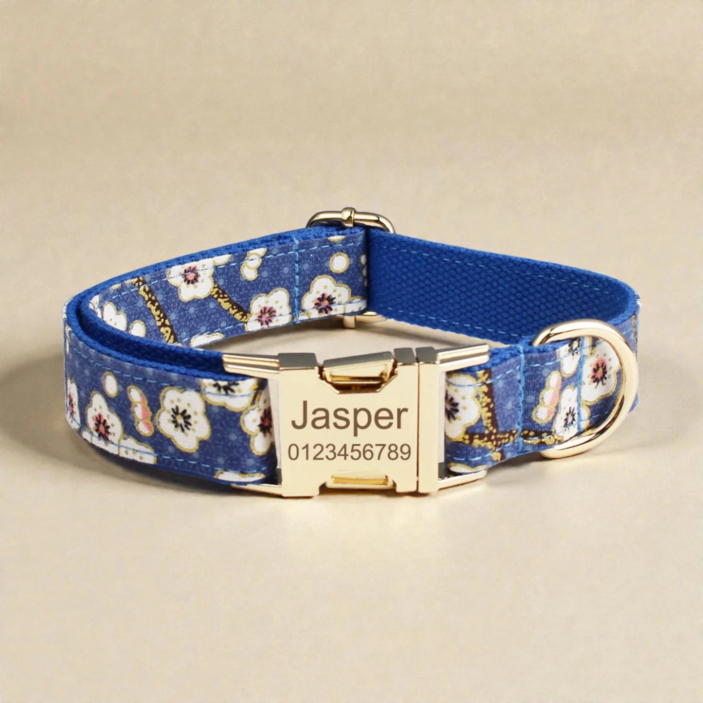 Blue floral-patterned dog collar with gold buckle and engraved nameplate on a beige background