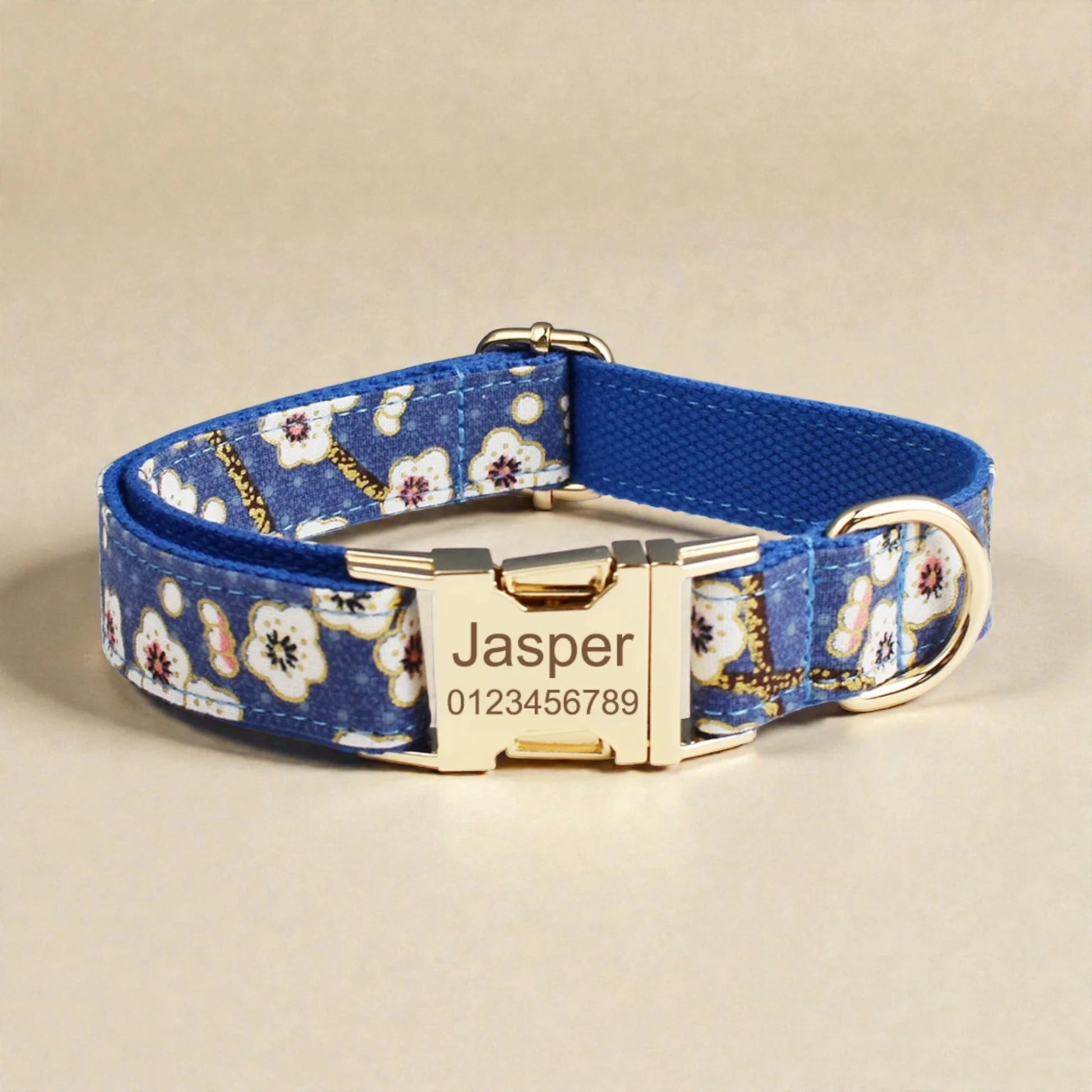 Blue floral-patterned dog collar with gold buckle and engraved nameplate on a beige background