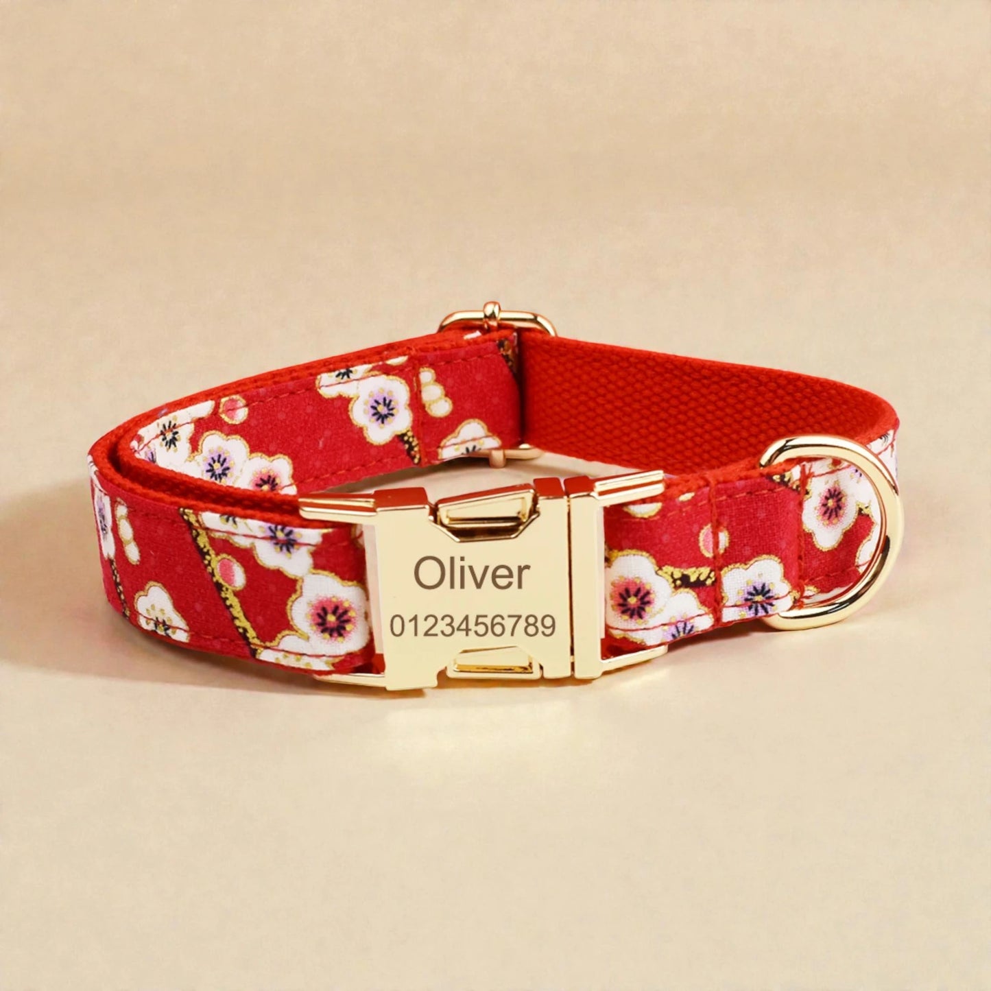 Red floral dog collar with gold buckle and engraved nameplate on a beige background