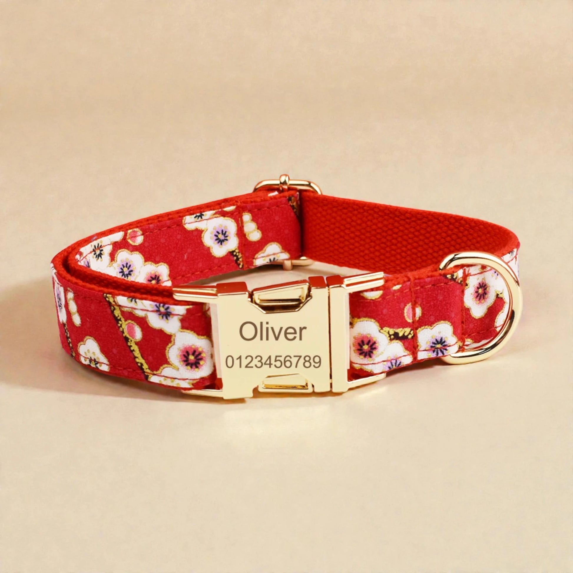 Red floral dog collar with gold buckle and engraved nameplate on a beige background