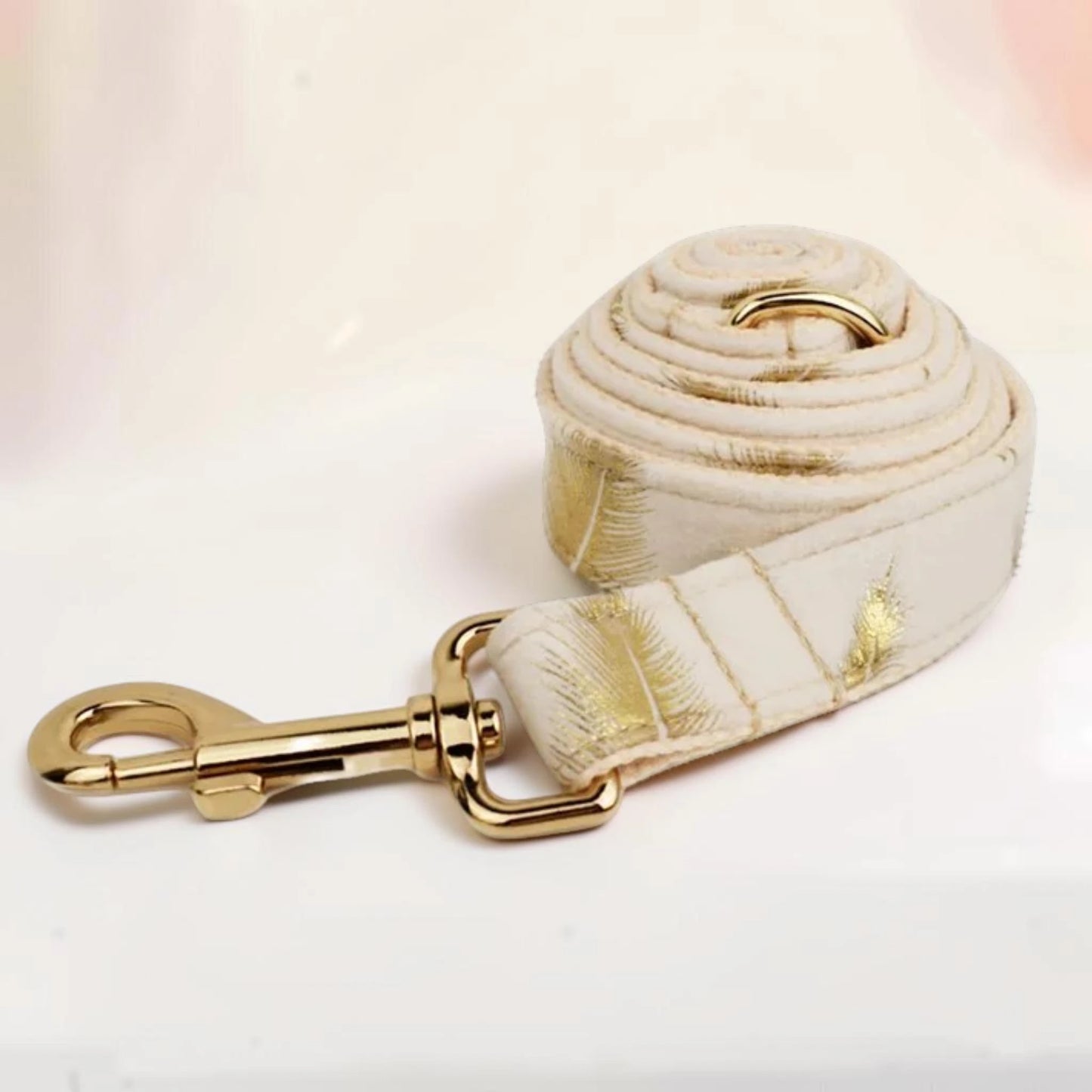A white dog lead with a golden feather pattern with a gold clasp.