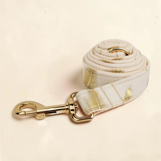 A white dog lead with a golden feather pattern with a gold clasp.