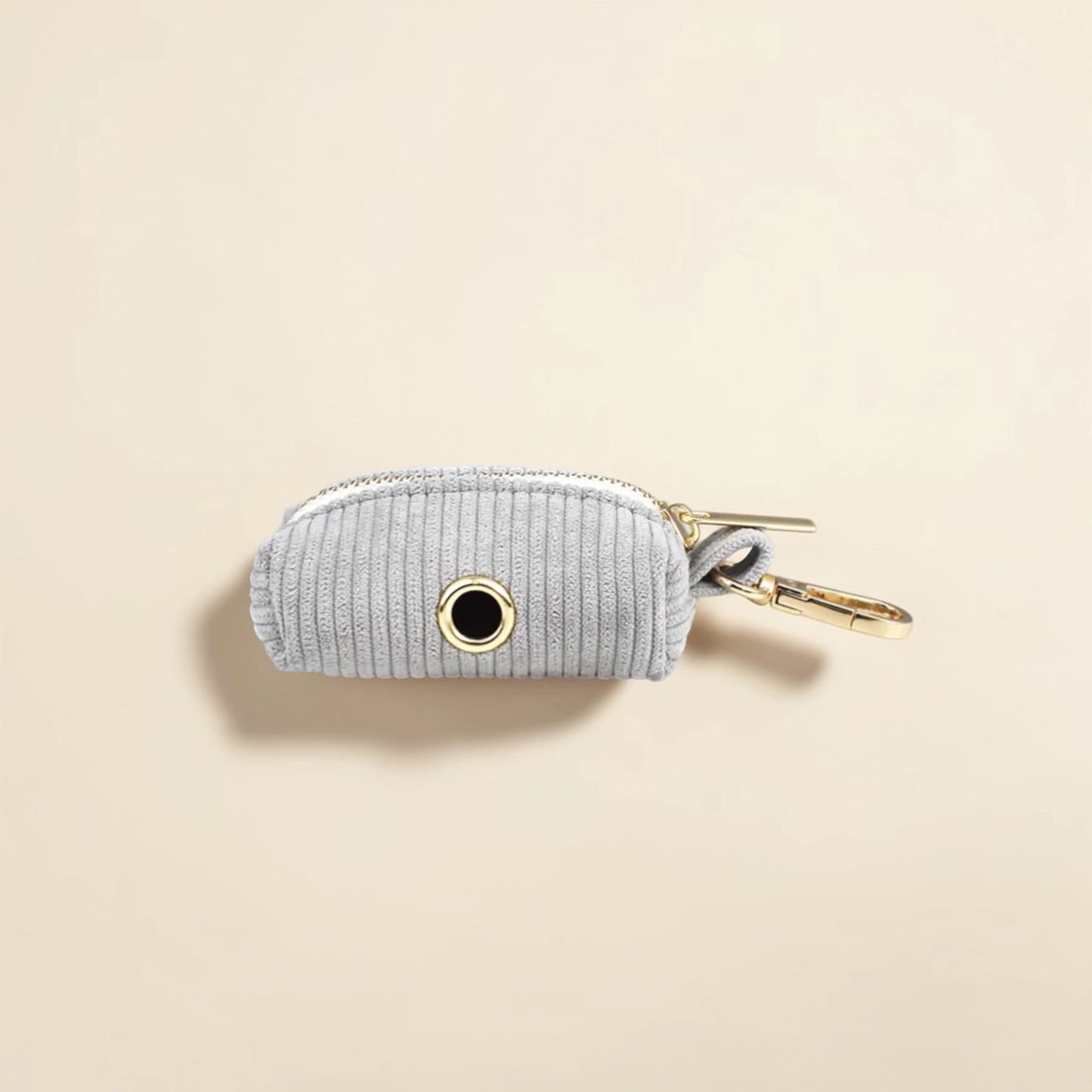 Light grey dog poop bag holder with gold zip on a beige background