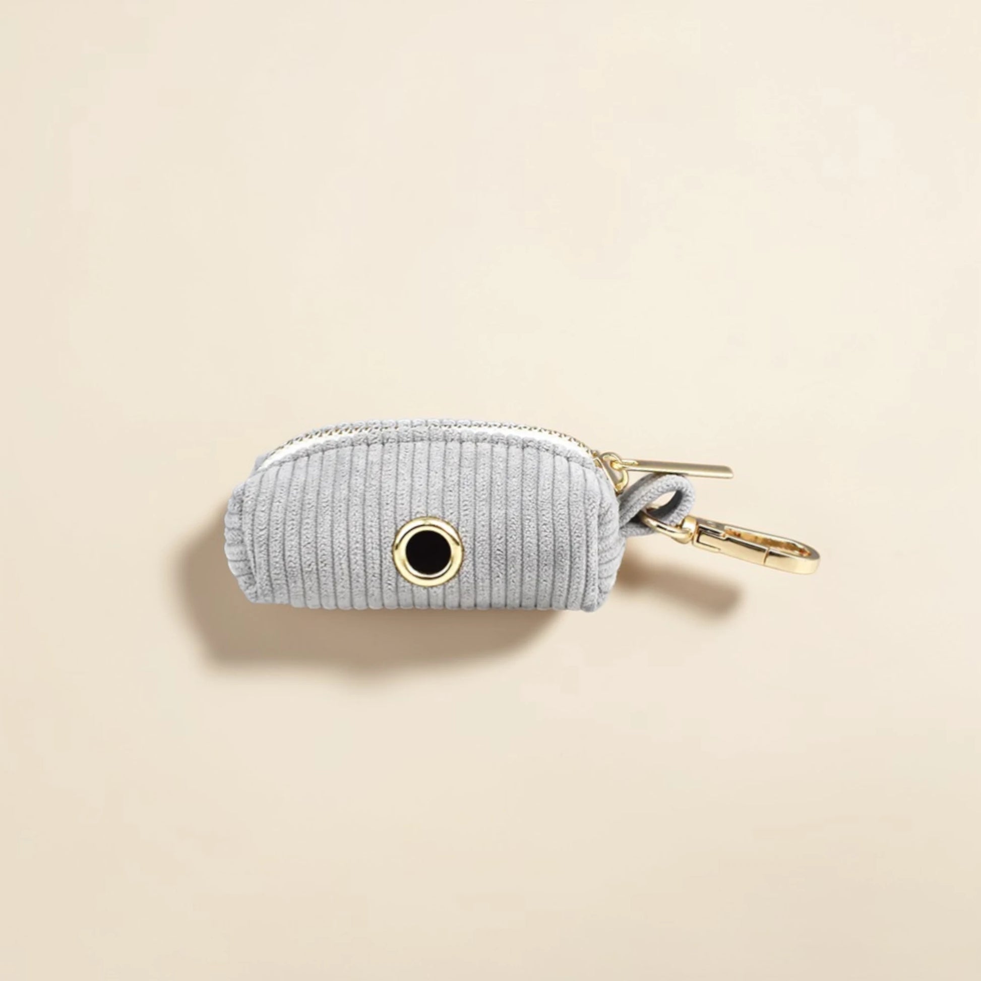 Light grey dog poop bag holder with gold zip on a beige background