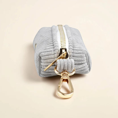 Light grey dog poop bag holder with gold zip and clip on a beige background