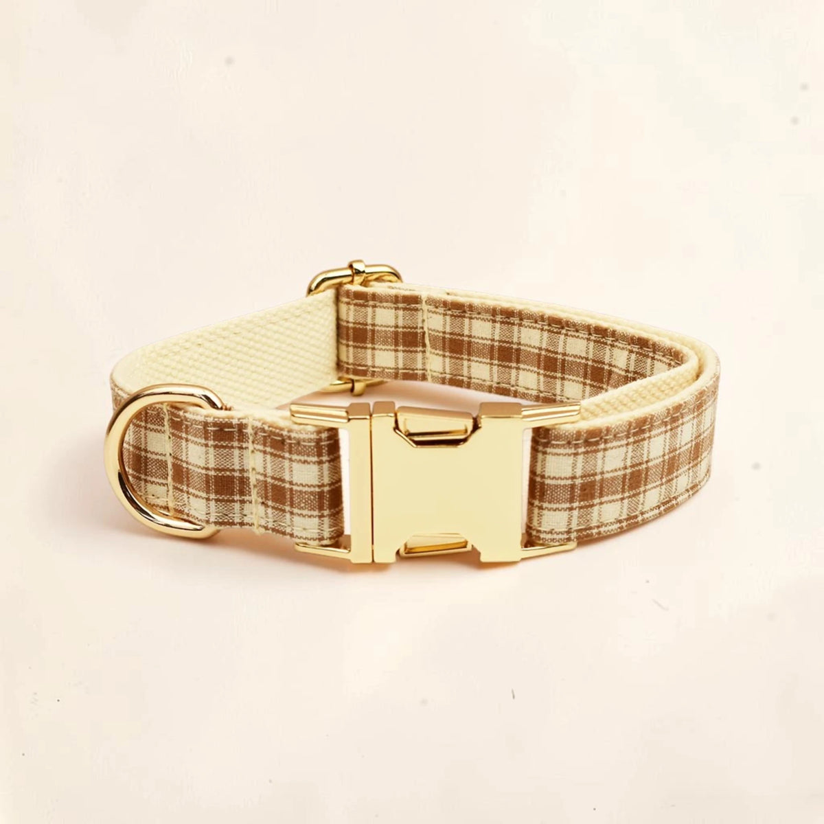 A dog collar with a brown and beige plaid pattern, a cream-colored inner lining, and a shiny gold buckle.