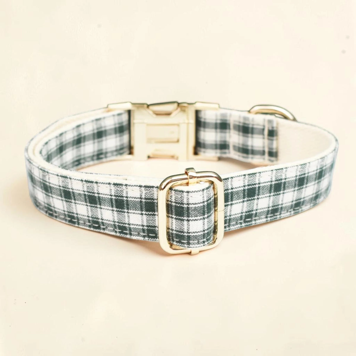 A dog collar with a green and white plaid pattern and a gold-tone metal buckle and D-ring.