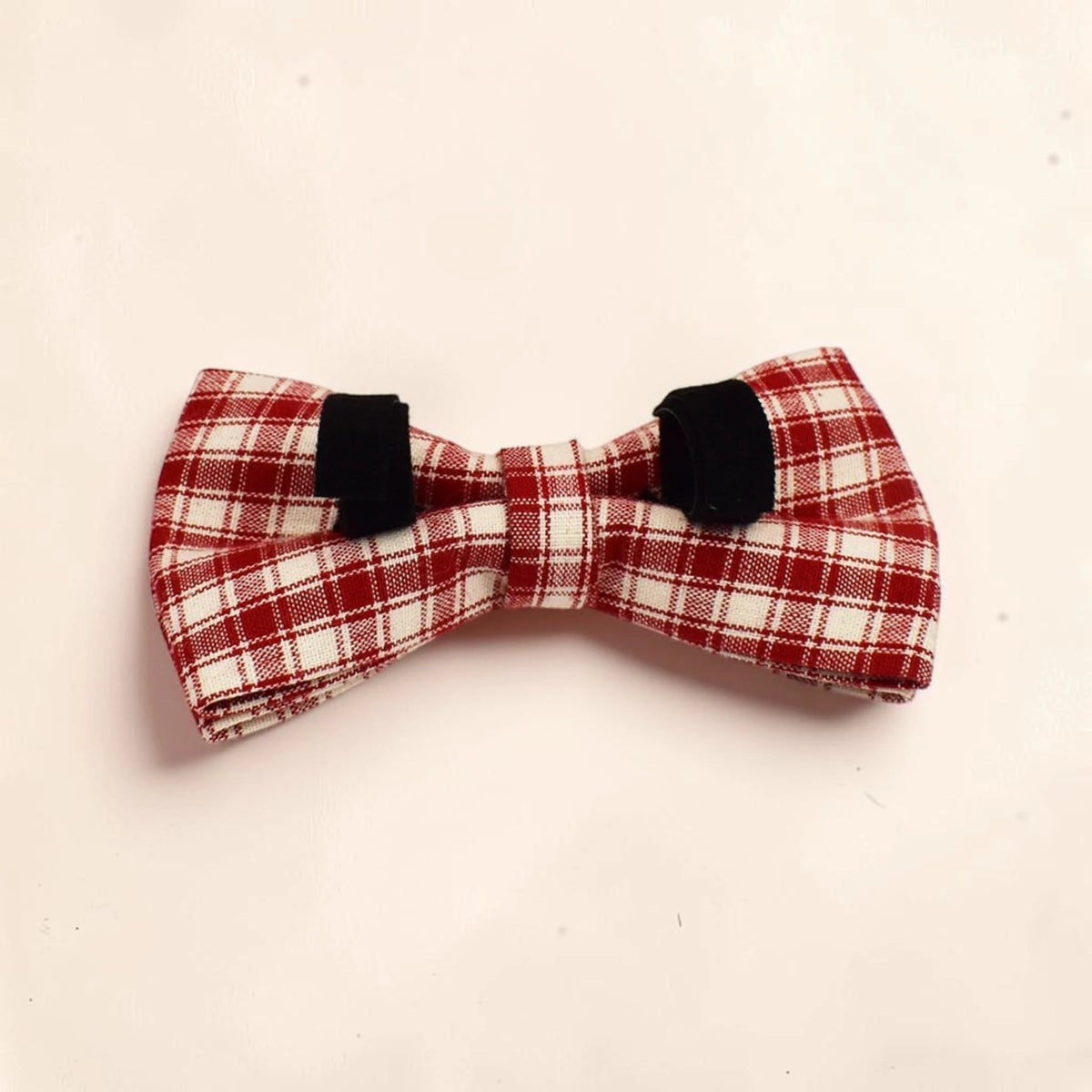 A red and white plaid detachable dog bow tie made of woven fabric.